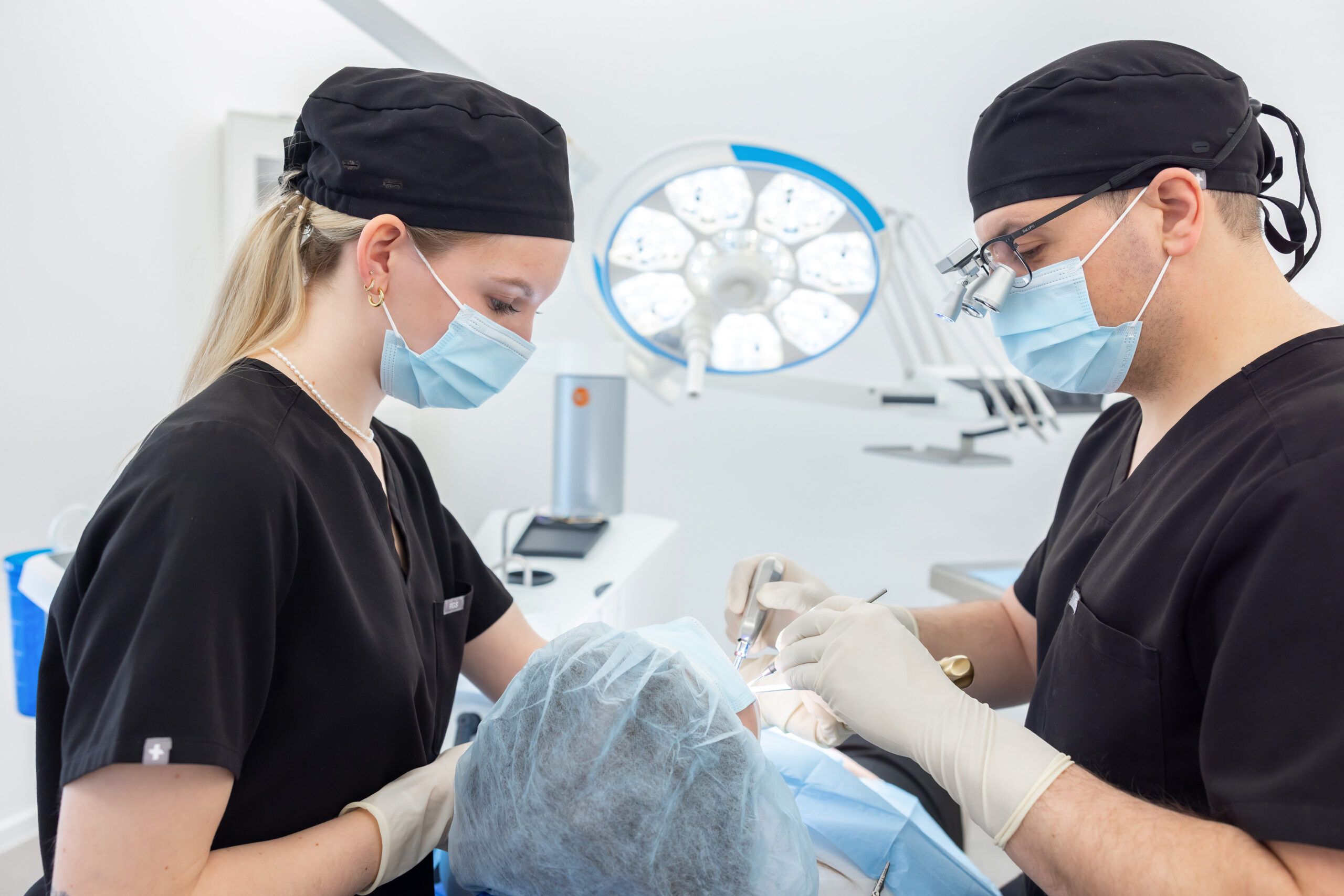 Zahnärztlicher Eingriff im Behandlungsraum der Praxis K1, der von Dr. Nemeth durchgeführt wird. Eine Mitarbeiterin assistiert ihm dabei.