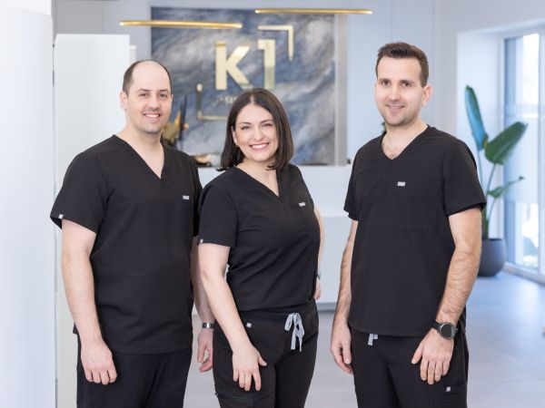 Dr. Nemeth, Dr. Korsos und Dr. Szabadi stehen vor dem Empfang der Praxis in Schärding. Das goldene Logo K1 prangt im Hintergrund über der Anmeldung.