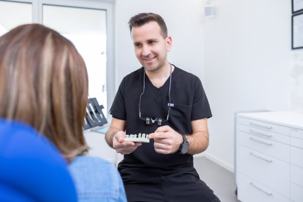Dr. Tamas Szabadi erläutert einer Patientin anhand eines Modells die Behandlung mit Veneers. Er hält das Modell in der rechten Hand und deutet mit der linken auf die Keramikschalen.