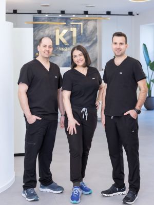 Dr. Nemeth, Dr. Korsos und Dr. Szabadi stehen vor dem Empfang der Praxis in Schärding, Frau Dr. Korsos steht zwischen den beiden Zahnärzten. Das goldene Logo K1 prangt im Hintergrund über der Anmeldung.