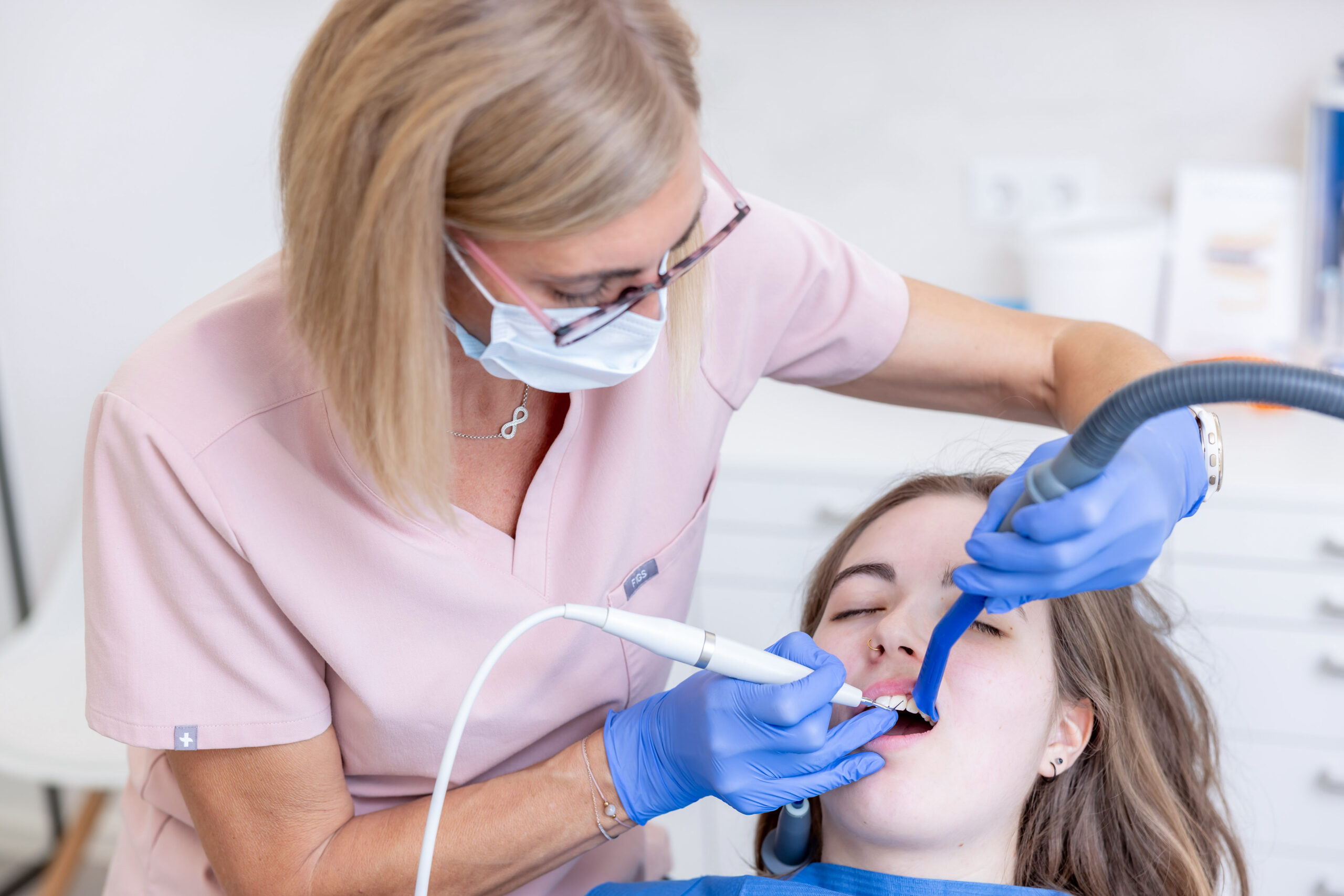 Eine Mitarbeiterin der Praxis K1 führt eine professionelle Zahnreinigung bei einer Patientin durch und ist hinter der Patientin platziert.